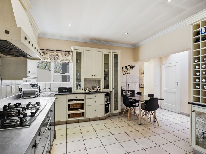 A well-appointed kitchen featuring cream cabinetry, a gas hob with extractor, integrated wine storage, and tiled flooring with an adjacent dining area.