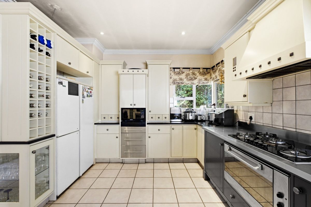 A functional kitchen featuring cream and dark grey cabinetry, stone countertops, a gas hob, built-in oven, and integrated wine storage.