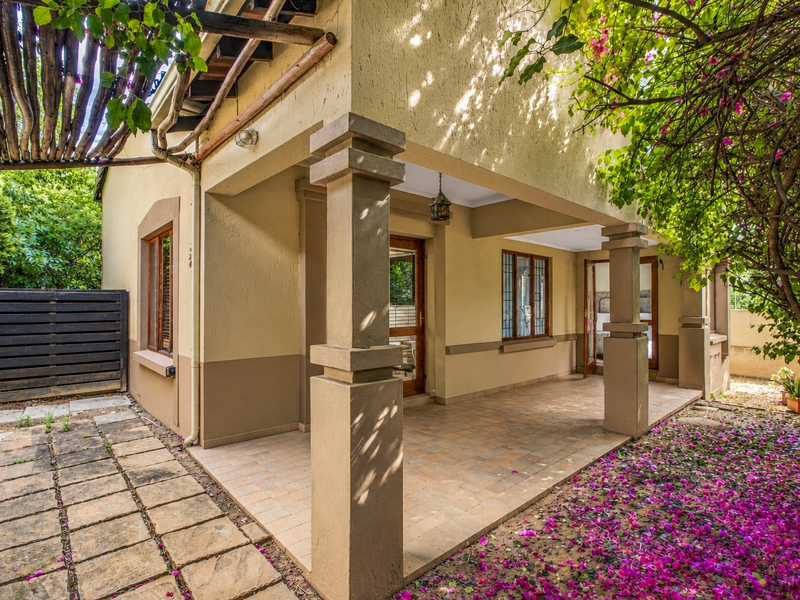 A covered patio area featuring structural pillars, tiled flooring, and a wooden pergola, providing direct access to the interior through timber-framed doors.