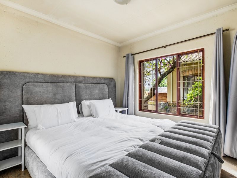 A well-lit bedroom featuring laminate flooring, coving, and a window fitted with security bars, offering a view of the exterior garden area.