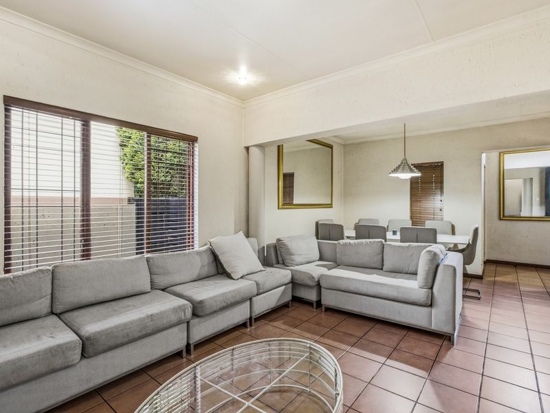 Spacious open-plan living and dining area featuring tiled flooring, neutral walls, and natural light through large windows with fitted venetian blinds.