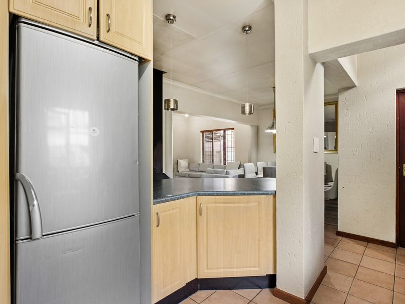Open plan kitchen area featuring laminate cabinetry and countertops, flowing into the living space with tiled flooring and pendant lighting.