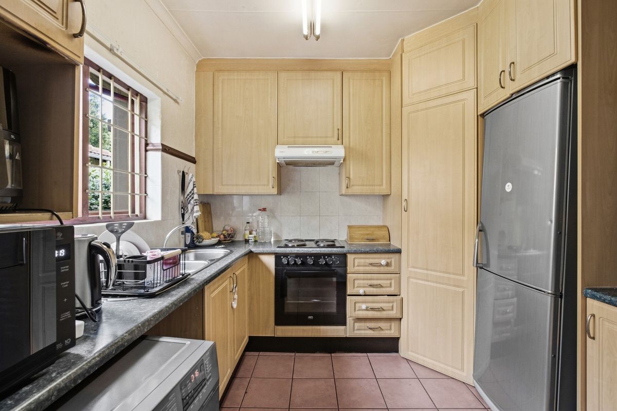 A functional kitchen featuring light wood-tone cabinetry, dark laminate countertops, built-in oven with hob, and tiled flooring with a window for natural light.