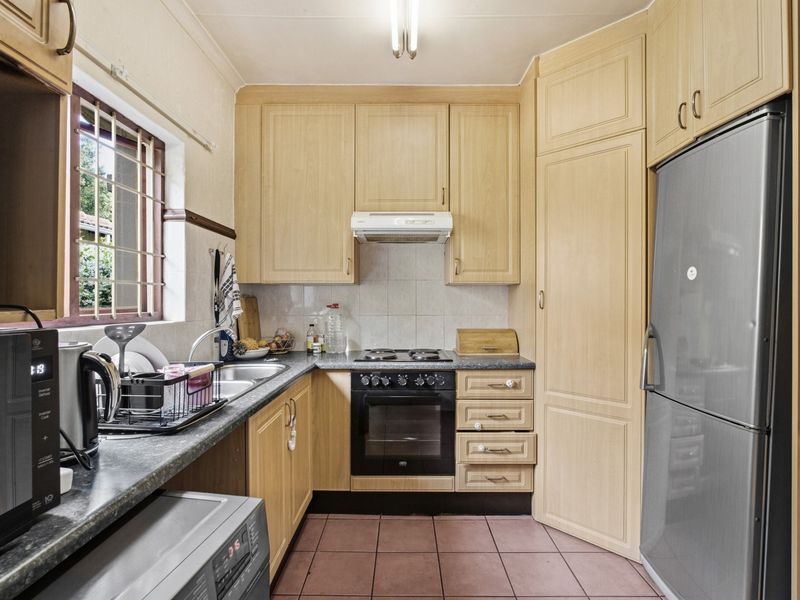 A functional kitchen featuring light wood-tone cabinetry, dark laminate countertops, built-in oven with hob, and tiled flooring with a window for natural light.