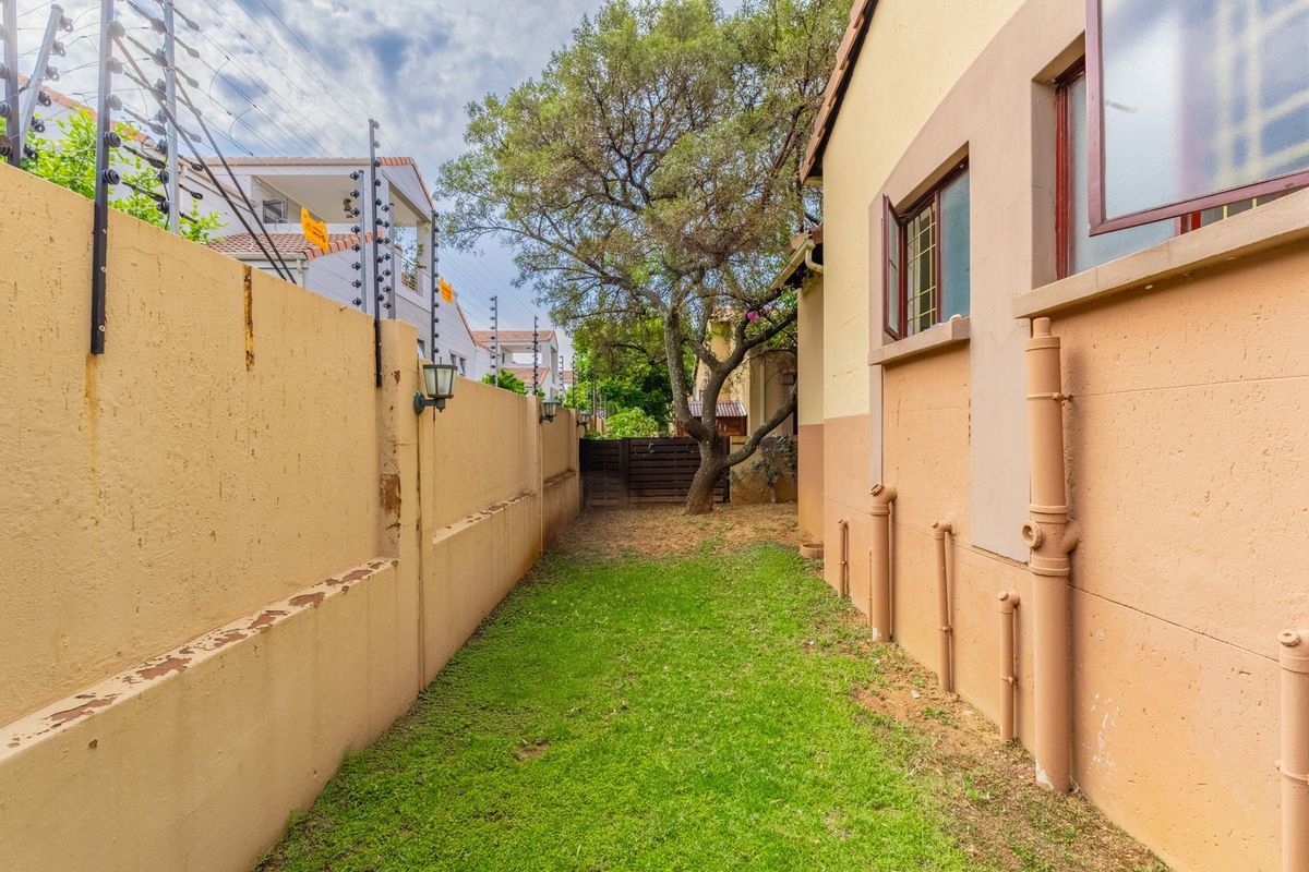 A narrow rear garden area featuring a lawn, boundary wall with electric fencing, and visible exterior plumbing pipes along the townhouse wall.