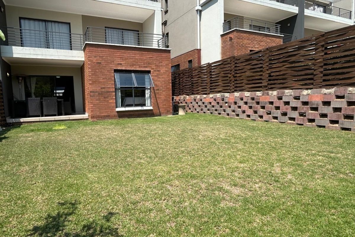 A well-maintained rear garden featuring a lawn, brick facade, retaining wall, and a private balcony with metal railings.