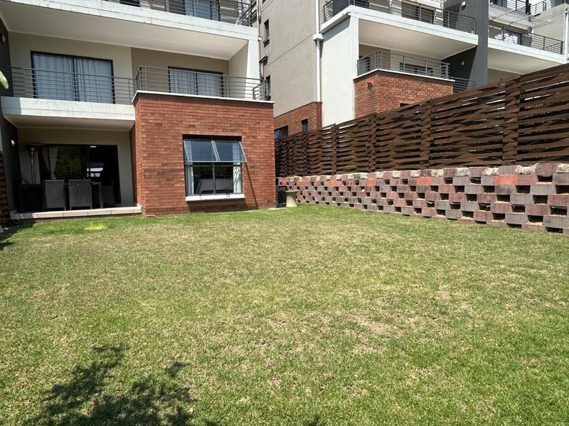 A well-maintained rear garden featuring a lawn, brick facade, retaining wall, and a private balcony with metal railings.
