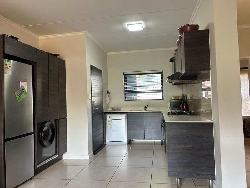A functional kitchen featuring dark wood-grain cabinetry, a gas hob with extractor, tiled flooring, and a clean, modern layout with integrated appliance spaces.