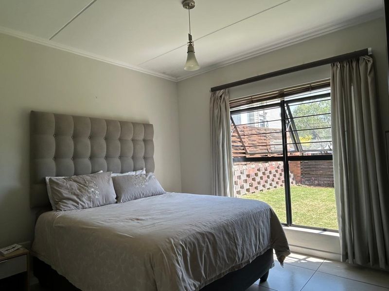 A well-lit bedroom featuring tiled flooring, a large top-hung window with curtain rails, and a neutral color palette.