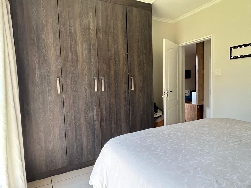 A bedroom featuring dark wood-grain built-in cupboards and neutral tiled flooring, with a doorway leading to an adjacent living space.