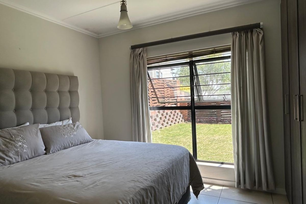 A well-lit bedroom featuring tiled flooring, a built-in wardrobe, and a large window with security bars overlooking a private garden area.