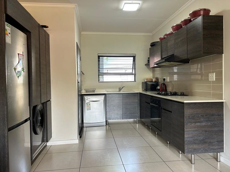Modern kitchen featuring dark wood-grain cabinetry, integrated appliances, tiled flooring, and a functional layout with ample counter space.