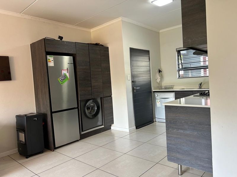 Modern kitchen featuring dark wood-look cabinetry, stone countertops, integrated laundry appliances, and tiled flooring in an open-plan layout.