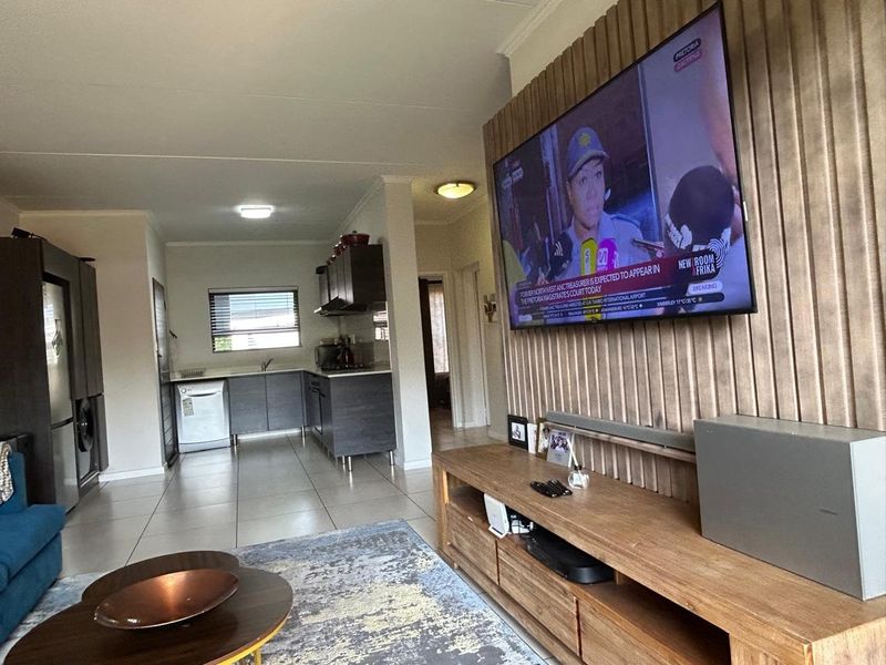 An open-plan living and kitchen area featuring modern cabinetry, tiled floors, and a feature wall with a mounted television.