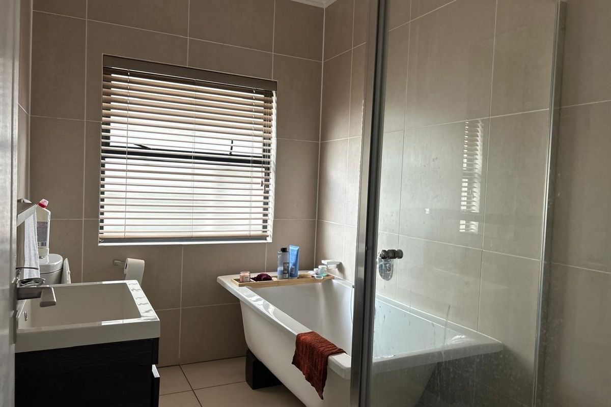 A modern bathroom featuring a freestanding bathtub, a glass-enclosed shower, and a vanity cabinet with neutral wall and floor tiling.