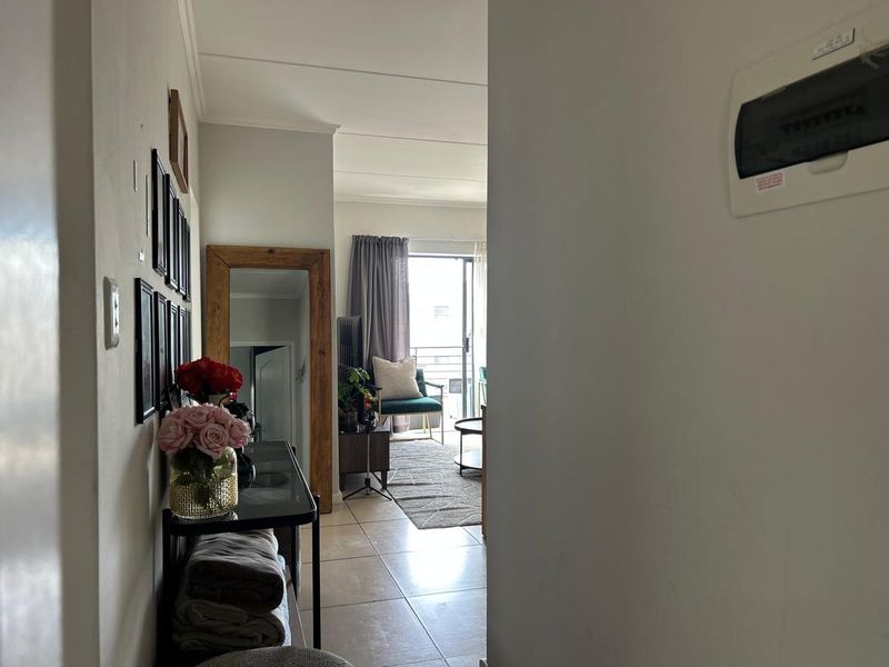 A view from the hallway looking through to the living area and balcony, featuring tiled flooring and a wall-mounted electrical distribution board.