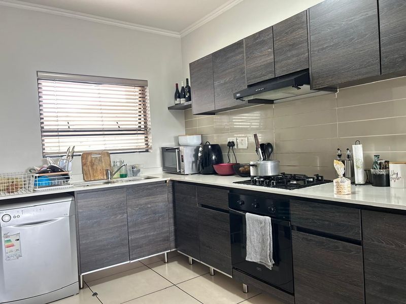 Modern kitchen featuring dark wood-grain cabinetry, gas hob, built-in oven, extractor fan, and tiled splashback with ample counter space.