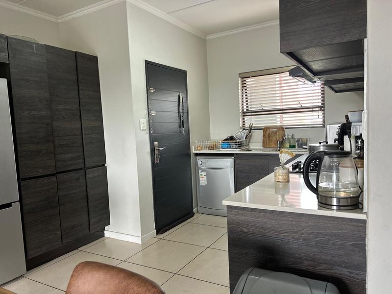 Modern kitchen featuring dark wood-grain cabinetry, stone countertops, integrated hob, extractor fan, and tiled flooring with direct access to an exterior door.