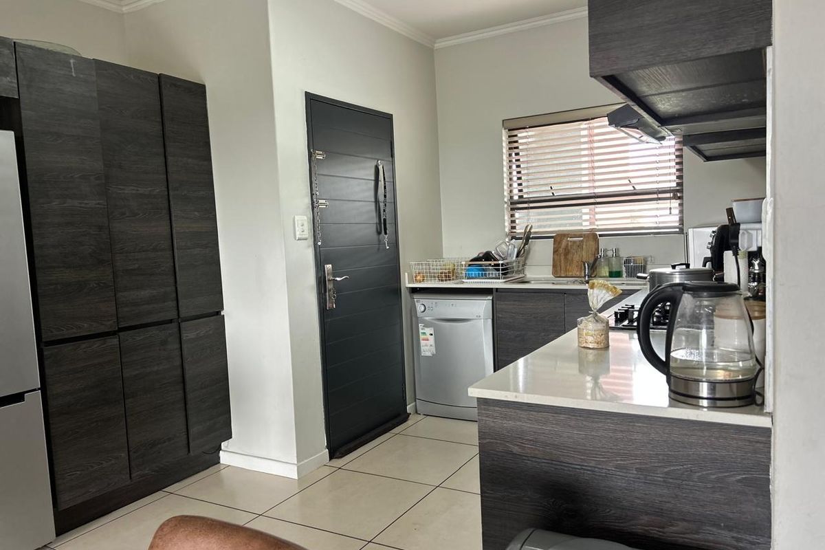 Modern kitchen featuring dark wood-grain cabinetry, stone countertops, integrated hob, extractor fan, and tiled flooring with direct access to an exterior door.