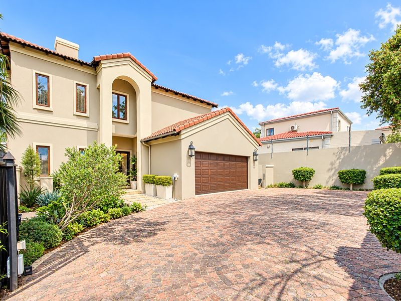 A well-maintained front exterior featuring a paved driveway, double garage, and attractive stucco facade with terracotta roof tiles.