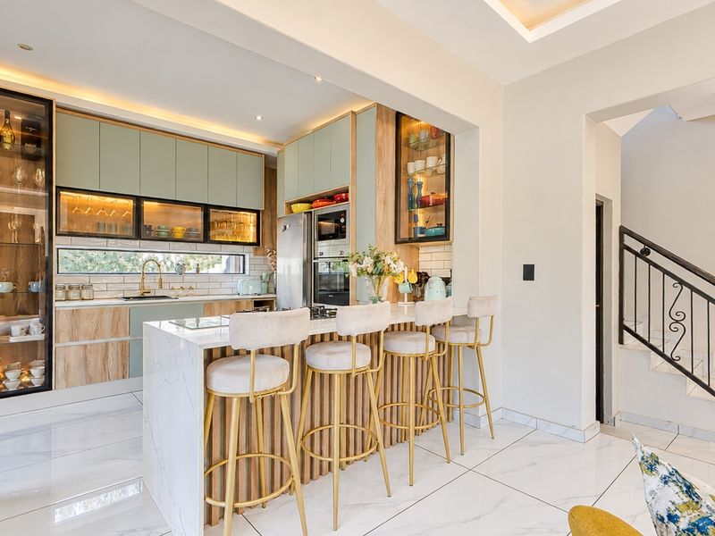 Modern kitchen featuring a marble-topped island, integrated cabinetry, built-in appliances, and elegant glass-front display units, seamlessly connected to the staircase area.