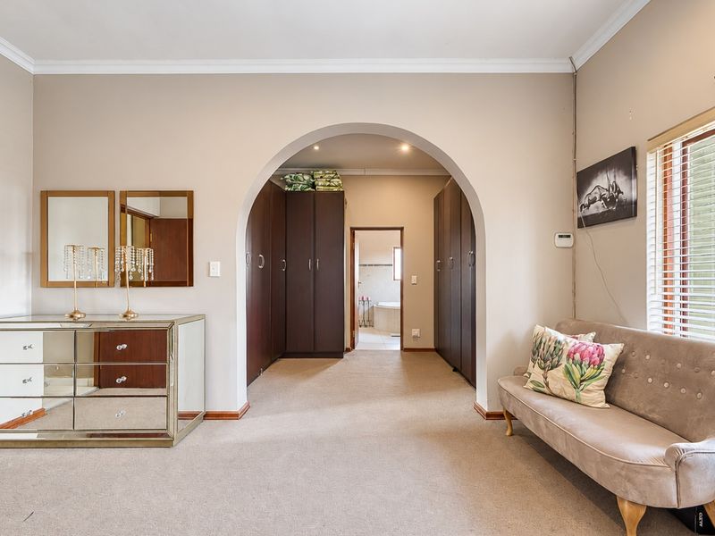 Spacious bedroom featuring built-in cupboards, a distinctive arched entryway leading to an en-suite, and neutral carpeting.
