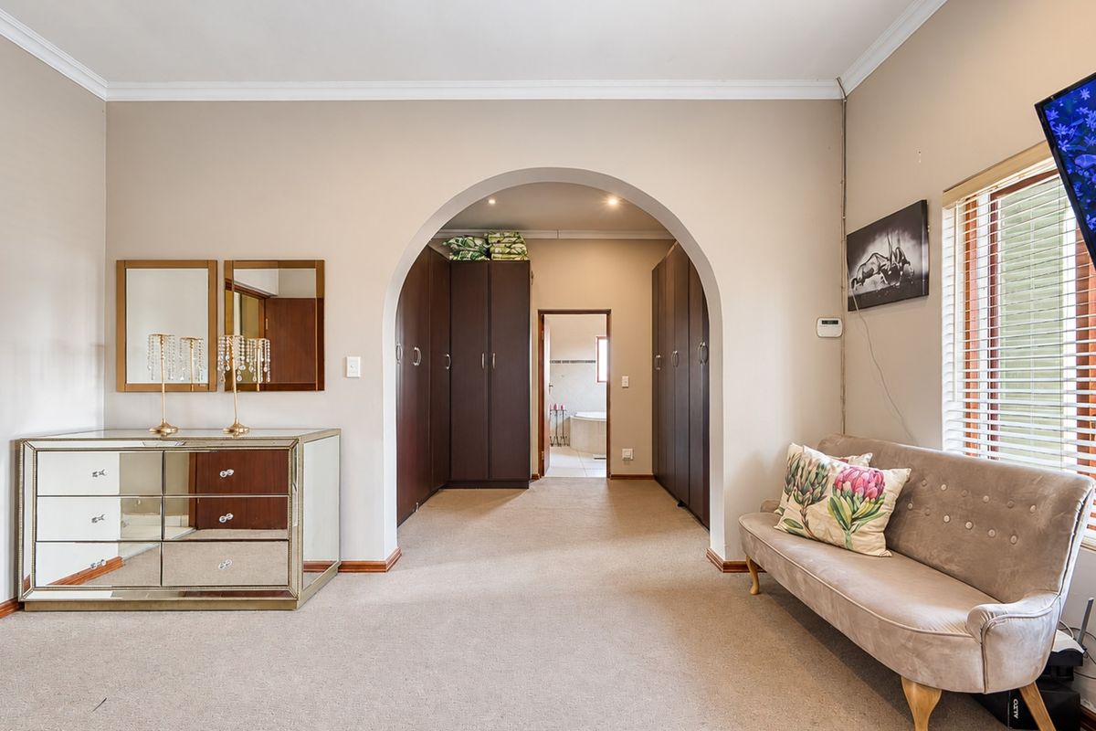 Spacious bedroom featuring built-in cupboards, a distinctive arched entryway leading to an en-suite, and neutral carpeting.