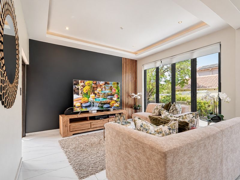 Modern living room featuring a striking timber slat accent wall, recessed ceiling with downlights, large format floor tiles, and expansive glass doors to the garden.