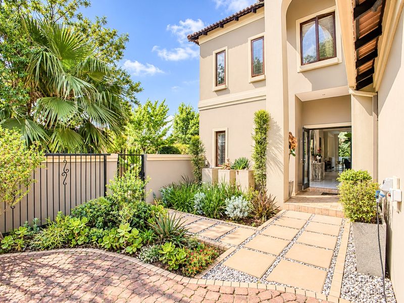 A well-maintained front entrance featuring a paved driveway, stone walkway, landscaped garden, and an elegant arched doorway leading into the home.