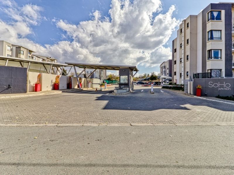 Secure entrance gatehouse and driveway access to the SoHo Junction apartment complex, featuring modern multi-story residential buildings and controlled perimeter access.