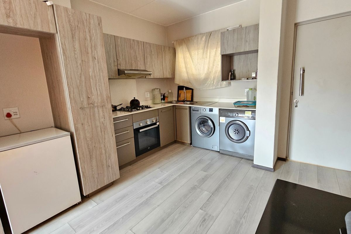 Compact kitchen featuring light wood-look cabinetry, built-in oven, gas hob, and integrated laundry space with durable laminate flooring.
