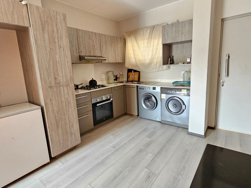 Compact kitchen featuring light wood-look cabinetry, built-in oven, gas hob, and integrated laundry space with durable laminate flooring.