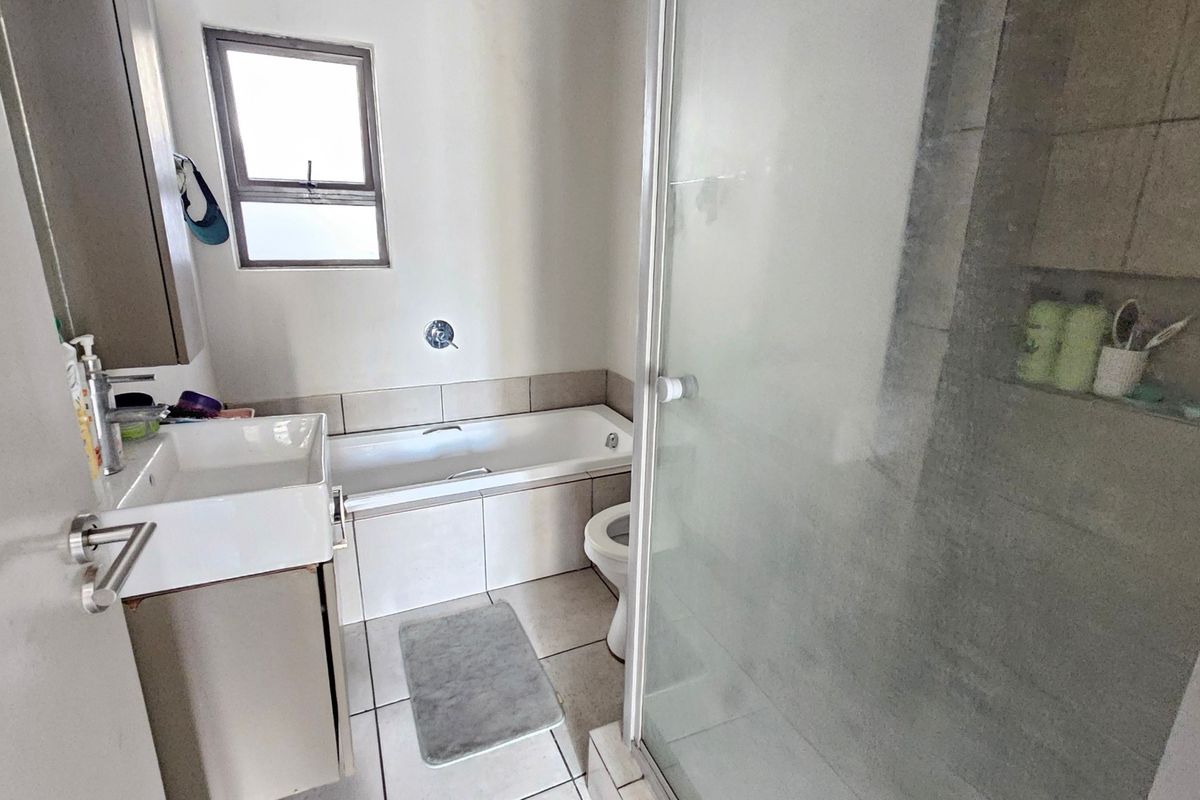 A functional bathroom featuring a built-in bathtub, a separate glass-enclosed shower, and a vanity basin with neutral tiling throughout.