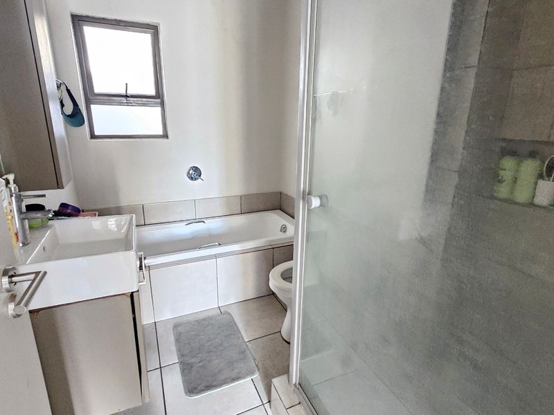A functional bathroom featuring a built-in bathtub, a separate glass-enclosed shower, and a vanity basin with neutral tiling throughout.
