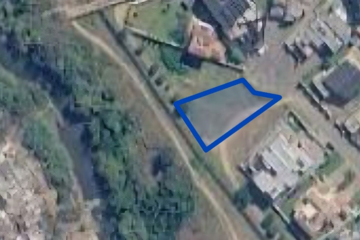 An aerial view of a vacant residential plot highlighted in blue, situated within a developed neighborhood area.