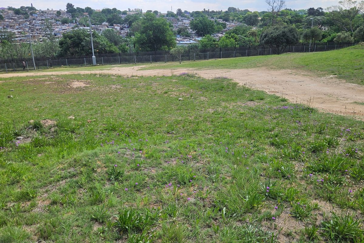 An elevated view overlooking a vacant residential plot with natural grass coverage and perimeter fencing, set against a suburban landscape.