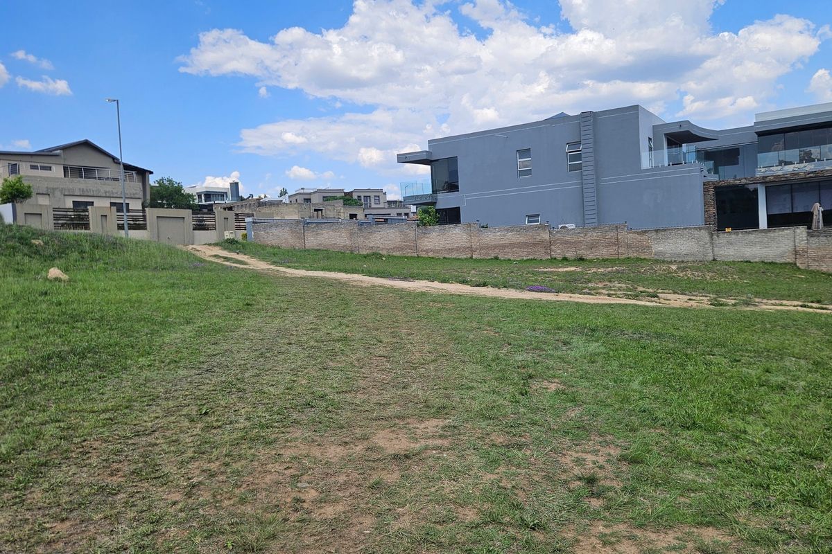 A vacant residential plot featuring a grass lawn and boundary wall, situated in a developed neighborhood.