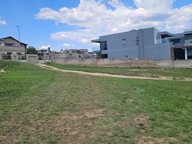 A vacant residential plot featuring a grass lawn and boundary wall, situated in a developed neighborhood.