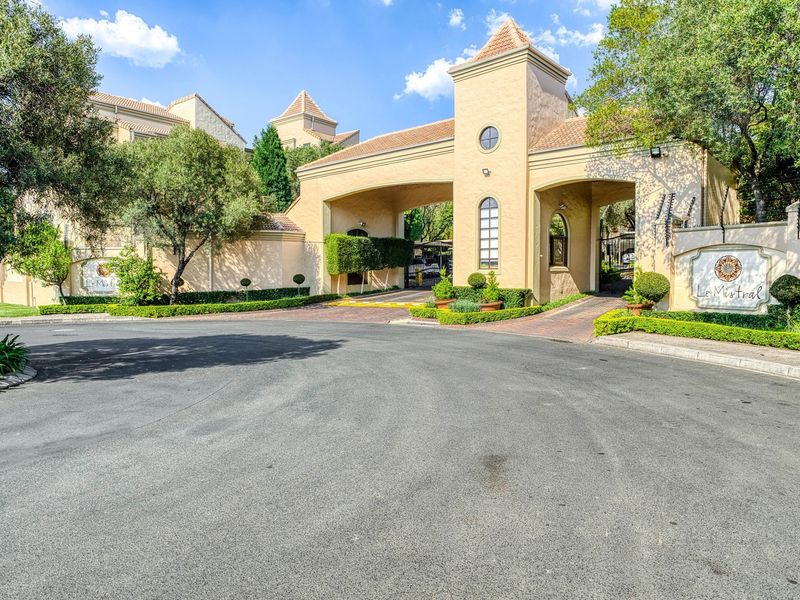 The main entrance to Le Mistral complex featuring a secure gated access point, paved driveway, and well-maintained landscaped gardens.