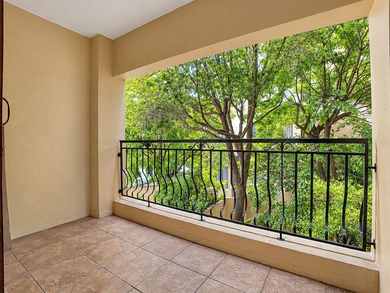 A private covered balcony featuring tiled flooring and a decorative wrought iron balustrade, offering a pleasant outlook onto mature trees.