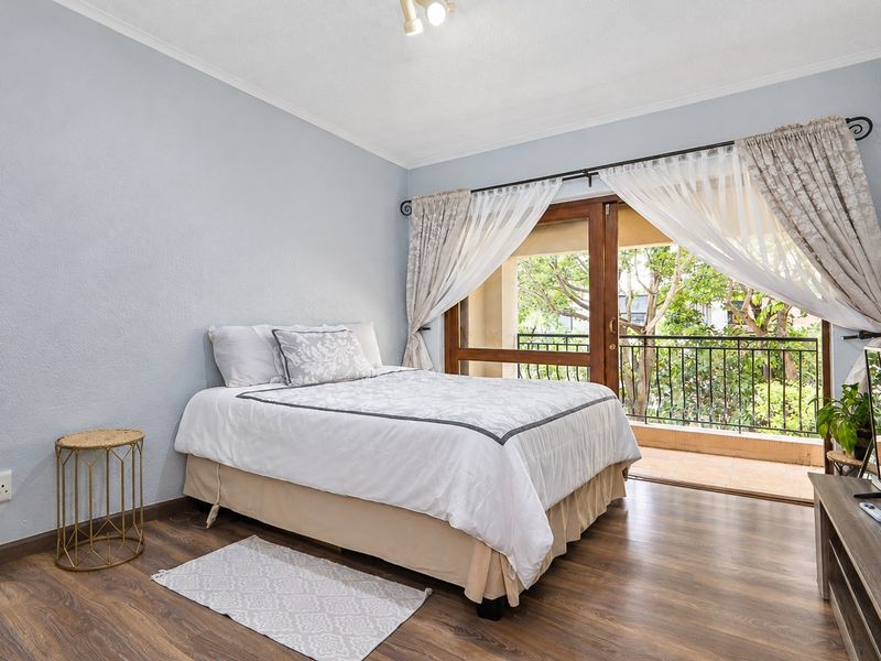 A well-lit bedroom featuring laminate flooring and direct access to a private balcony through sliding glass doors.