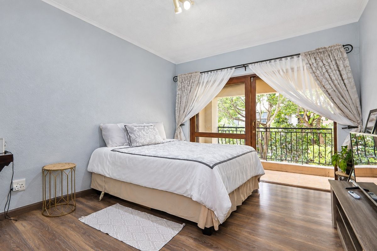 A well-lit bedroom featuring laminate flooring and direct access to a private balcony through sliding glass doors.