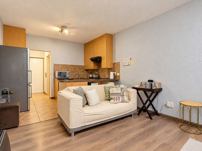 Open-plan living area featuring a compact kitchen with built-in cabinetry, laminate flooring, and a tiled backsplash, creating a functional and connected living space.