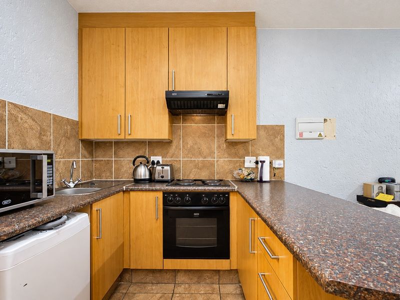 Compact kitchen featuring wooden cabinetry, laminate countertops, tiled backsplash, and built-in oven with extractor fan.
