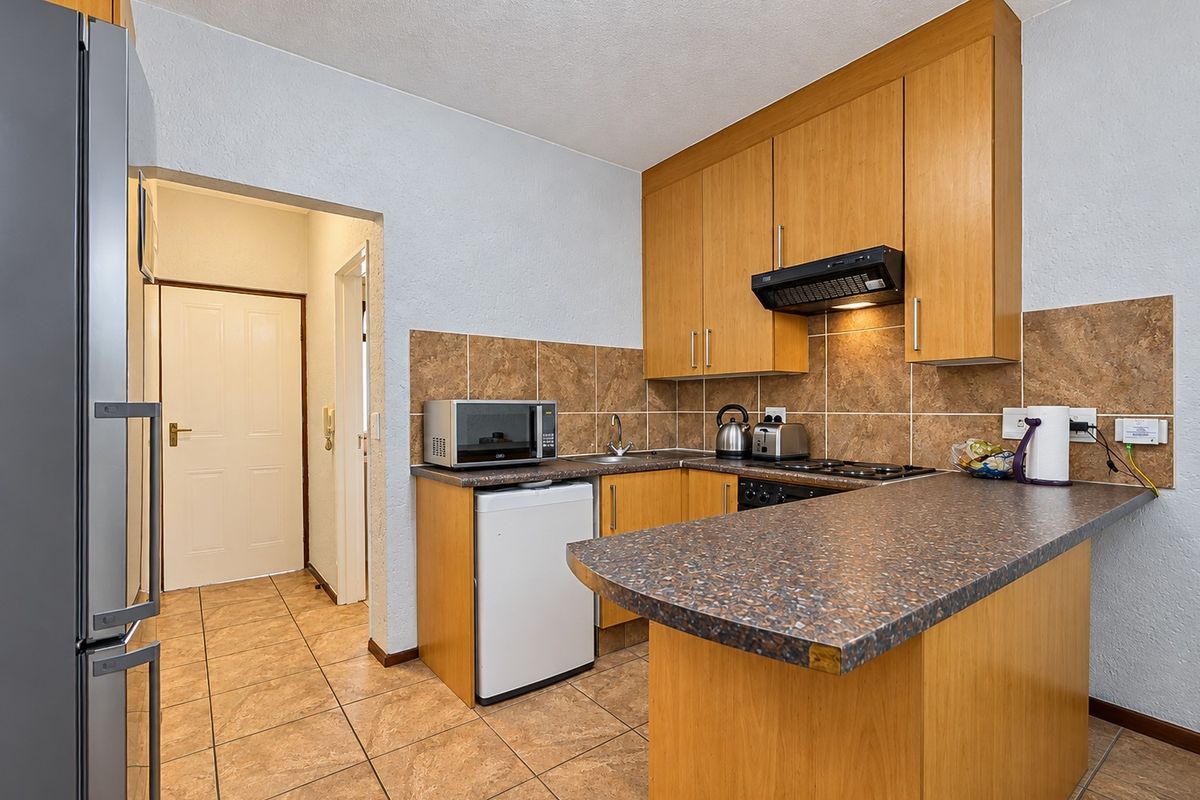 Compact kitchen featuring wood-look laminate cabinetry, tiled backsplash, and a breakfast bar counter, providing a functional layout with essential built-in appliances.