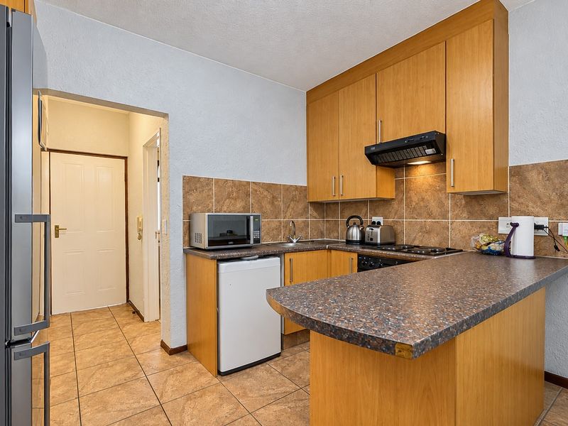 Compact kitchen featuring wood-look laminate cabinetry, tiled backsplash, and a breakfast bar counter, providing a functional layout with essential built-in appliances.
