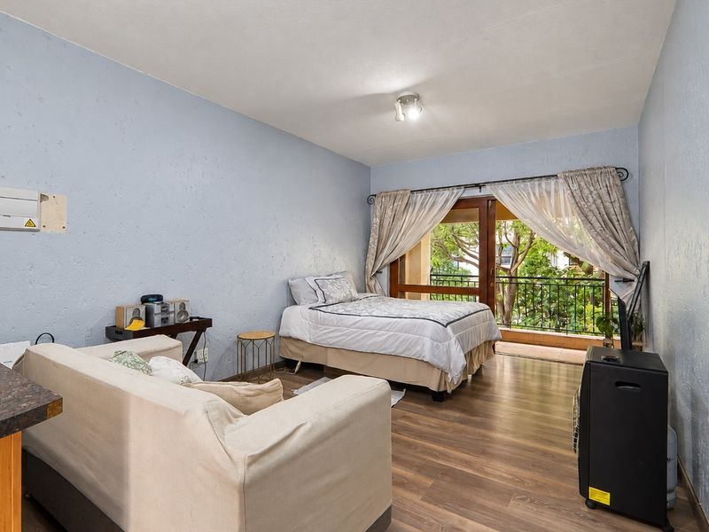Open-plan living and bedroom area featuring laminate flooring, textured walls, and direct access to a private balcony through sliding glass doors.