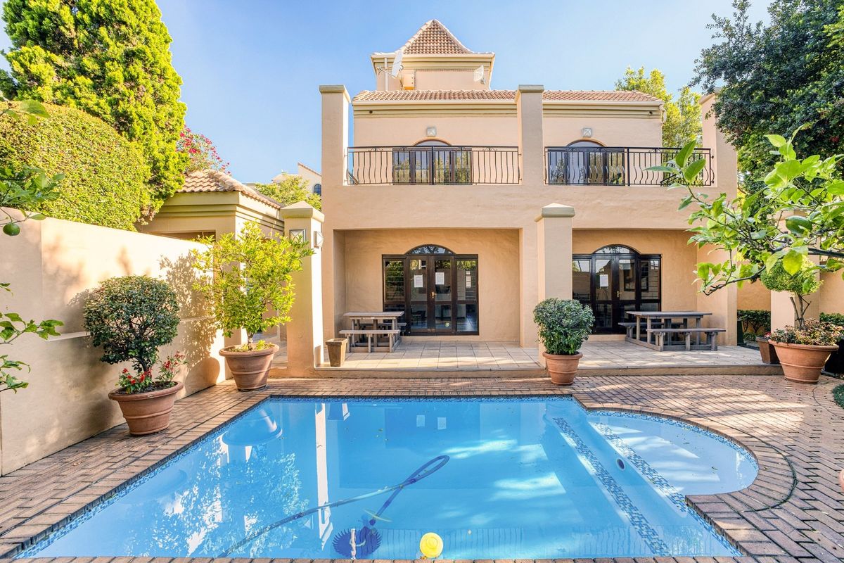 Rear view of the property featuring a private swimming pool, paved patio area, and an upper-level balcony with wrought iron railings.