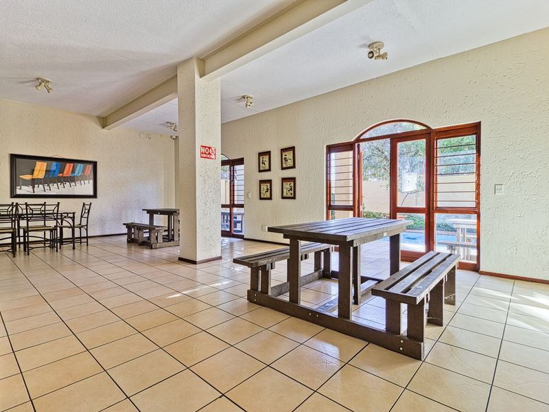 Spacious clubhouse area featuring tiled flooring, structural columns, and large arched wooden doors providing access to the outdoor pool area.