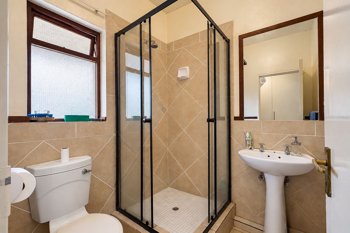 A functional bathroom featuring a shower enclosure, pedestal basin, toilet, and tiled finishes, providing a practical and well-maintained space.